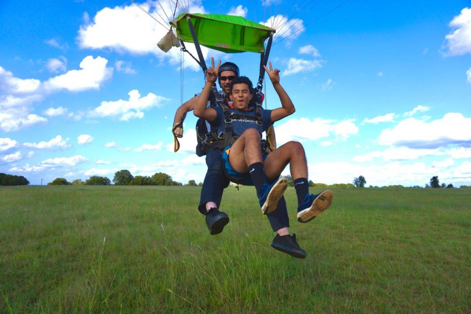 Male tandem skydiving student and instructor landing in a grass field after a tandem skydive at Texas Skydiving near Austin, TX