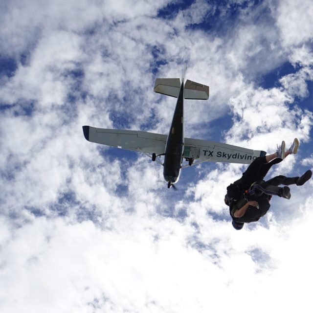 Tandem skydiving student and instructor in freefall with a Texas Skydiving airplane above them