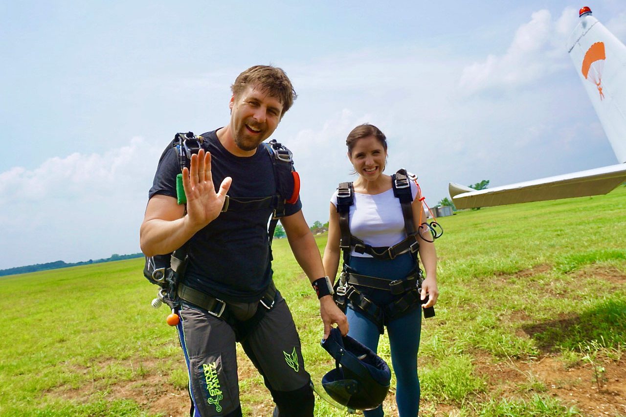Smiling tandem skydiving instructor and student wave at camera before boarding a plane