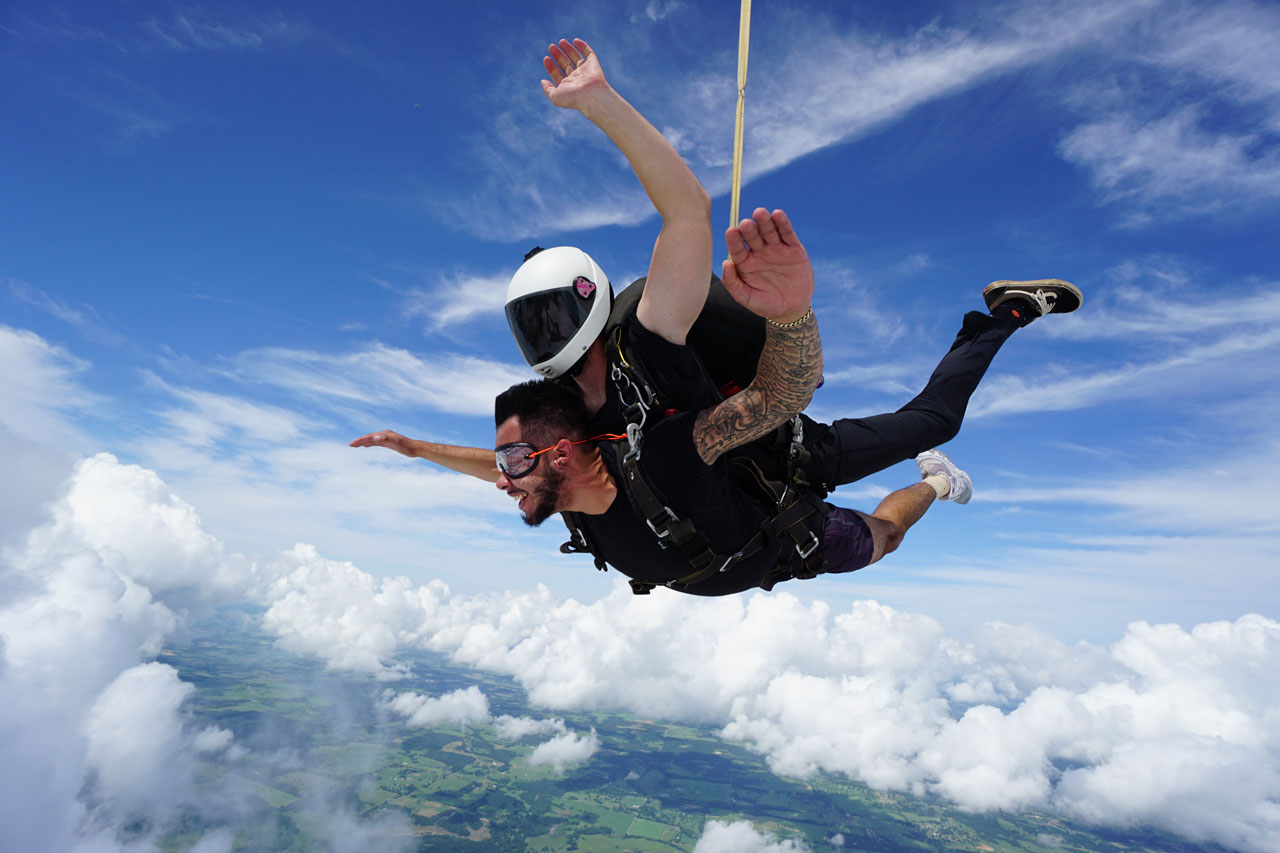 Male tandem skydiving student and instructor in freefall with blue sky background