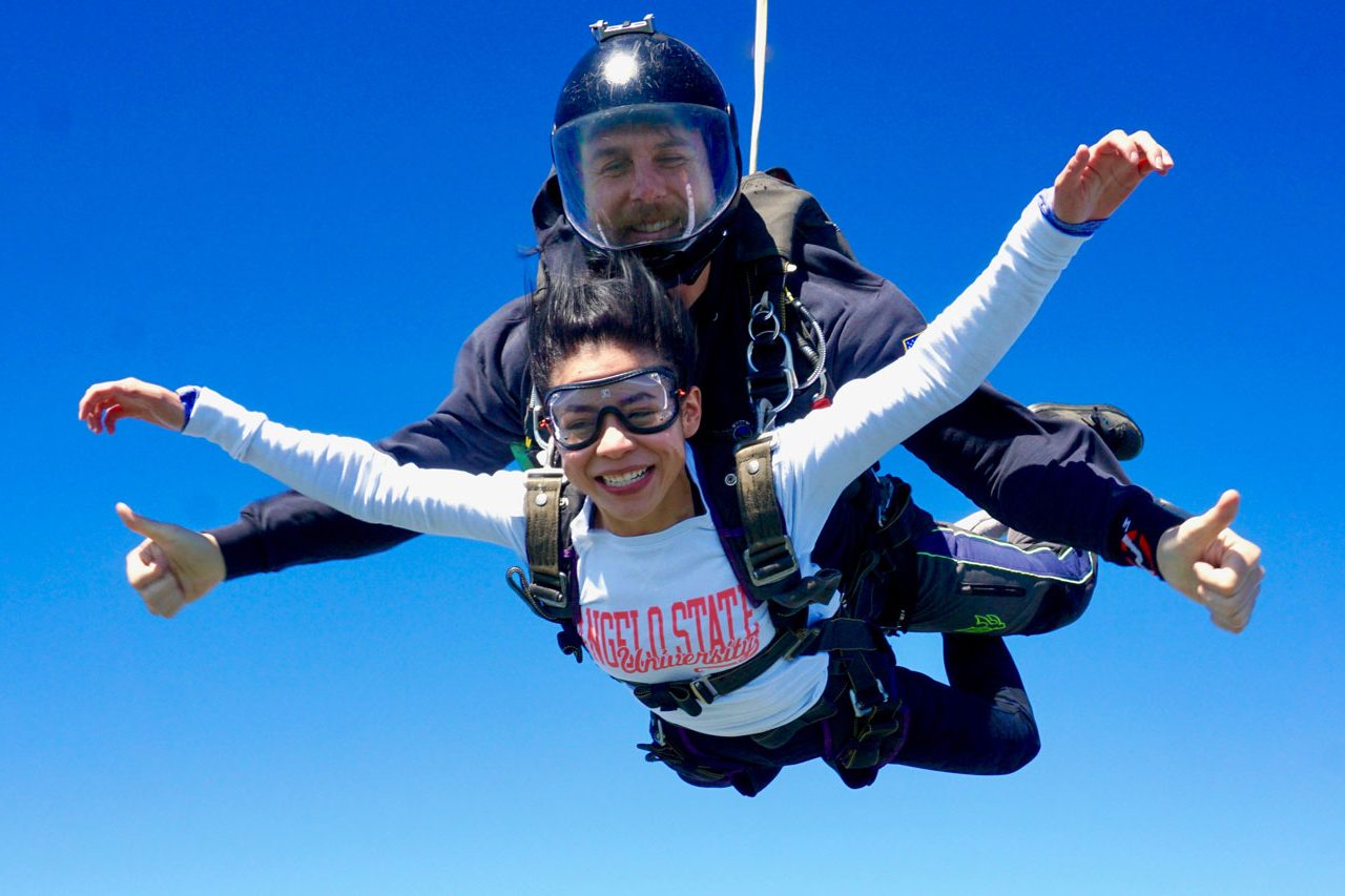 young woman with white college tshirt on smiles in skydiving freefall
