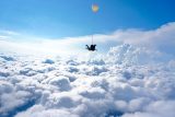 Tandem skydiving student and instructor in freefall with a blue sky background and fluffy white clouds below