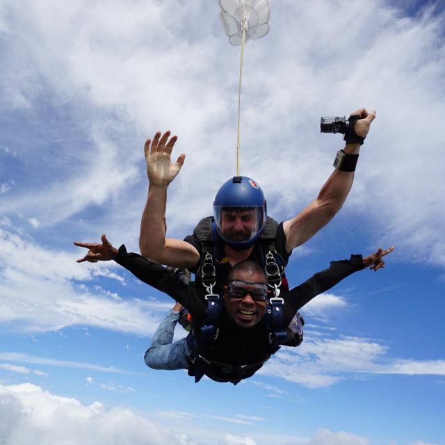 Tandem skydiving student and instructor in freefall with blue sky background