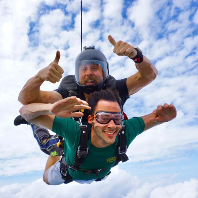 Young man wearing green t-shirt tandem skydiving for the first time at Texas Skydiving near Austin, TX