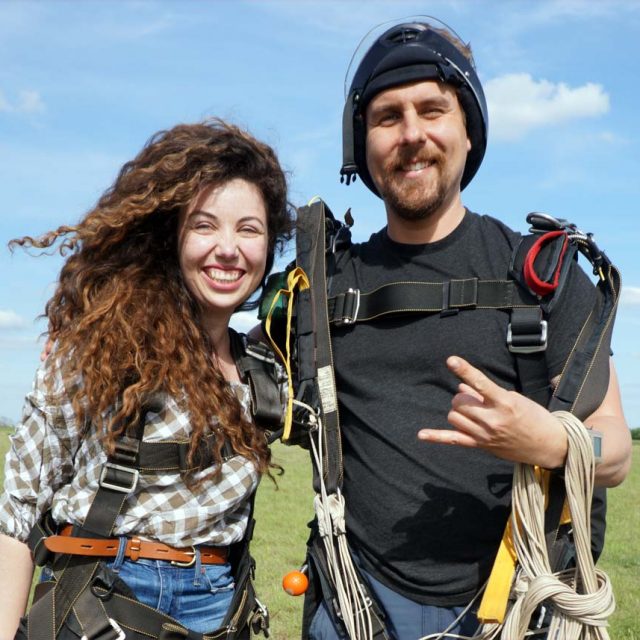 Young woman with dark curly hair poses with her instructor after a tandem skydive at Texas Skydiving near College Station, TX