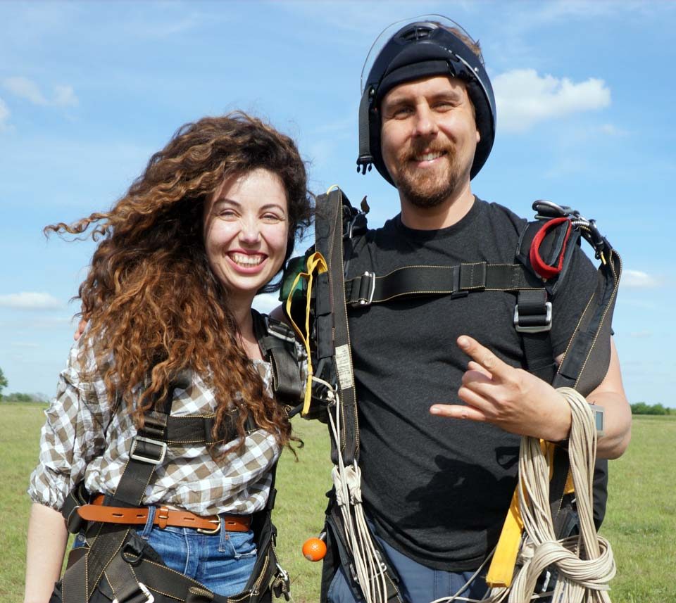 Young woman with dark curly hair poses with her instructor after a tandem skydive at Texas Skydiving near College Station, TX