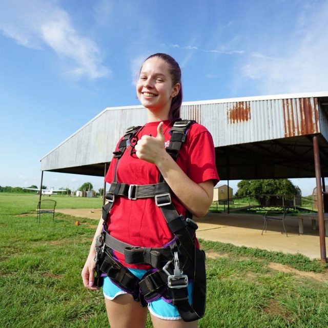Female tandem skydiving student in skydiving harness giving a thumbs up to camera before her jump at Texas Skydiving