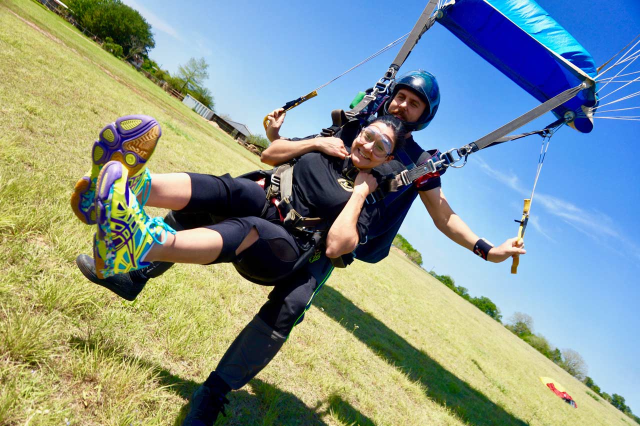 Female tandem student in black t-shirt landing in a grassy field at Texas Skydiving near Austin, TX