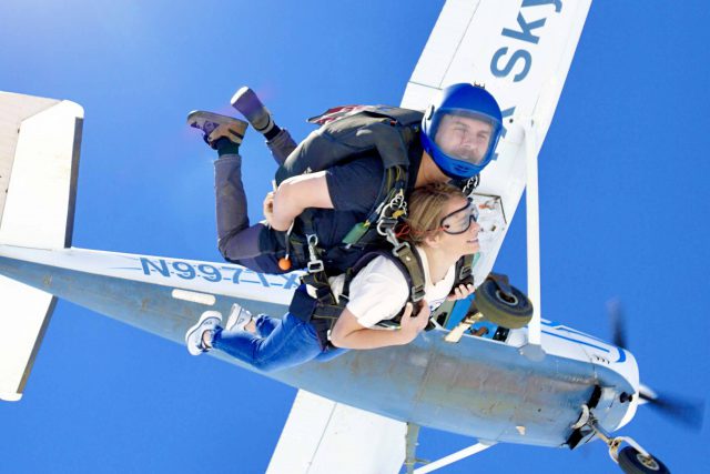 Tandem skydiving instructor and student skydiving near Austin, TX with plane and blue sky in background