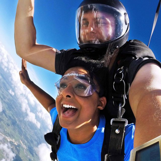 Young woman in blue t-shirt smiling at camera while in freefall during a tandem skydive near Austin, TX