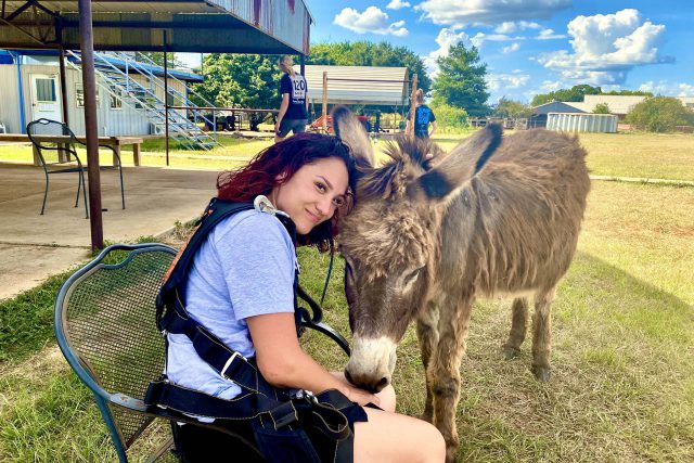 Female tandem skydiving student sits in a chair while petting a donkey at Texas Skydiving near College Station, TX